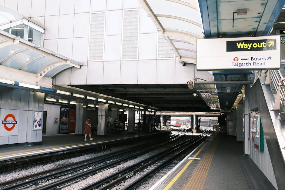 Inside the London Underground station at Cockfosters, the platform features white tiled walls with signage including a roundel symbol for Leicester Square, and a black door with various warning signs