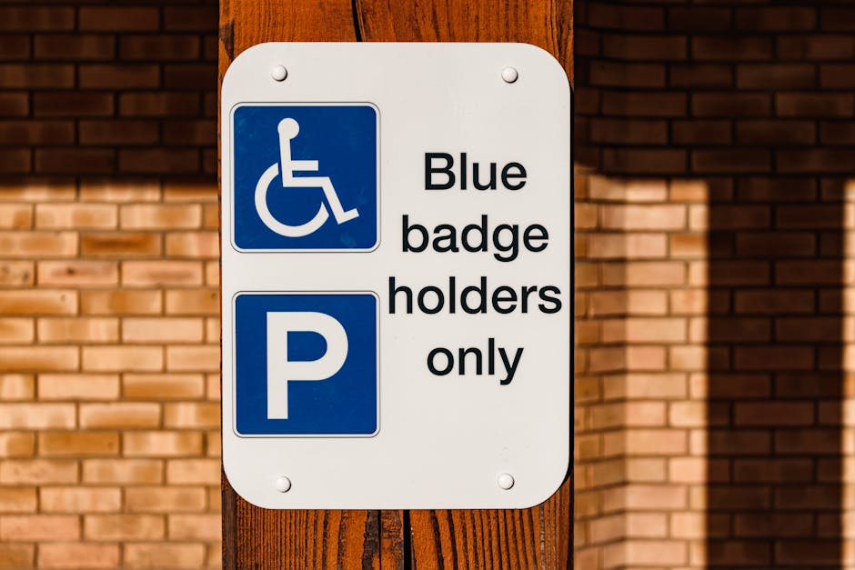 A vertical metal signpost installed on a sidewalk under a tree with bare branches, displaying a reserved parking sign for disabled individuals with a blue wheelchair symbol and the text 'RESERVED PARKING' in green. Below this, a secondary sign indicates 'VAN ACCESSIBLE' in green. The background features an overcast sky and leafless tree branches, with no vehicles or moving equipment visible. The scene is part of an urban area where house removals and moving services, such as those offered by Man with Van Cockfosters, could operate, particularly in contexts involving parking regulations and permits for home relocation logistics.